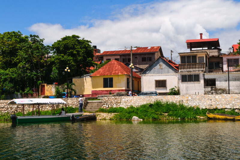 Waterfront buildings in Flores with red metal roofs, a stone seawall, and wooden boats moored along Lake Petén Itzá