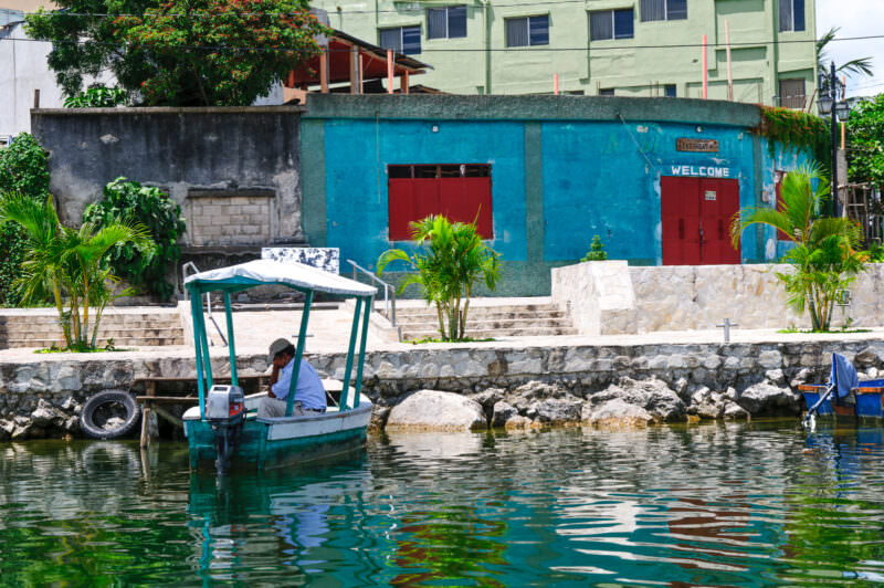Bright turquoise building with red doors along the waterfront of Flores, with a small covered boat moored at the stone seawall in Lake Petén Itzá