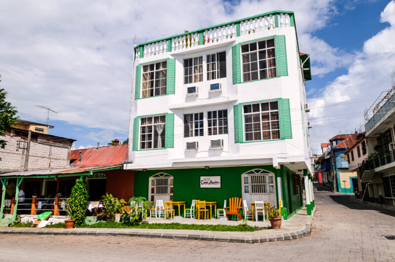 Hotel Casa Amelia, a white three-story building with green shutters and trim, fronted by a terrace with yellow chairs along the waterfront in Flores