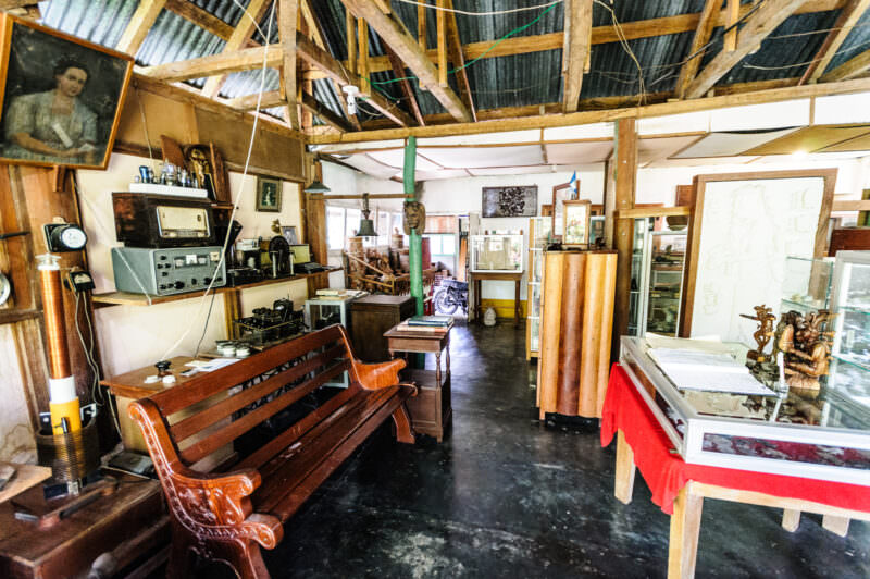 Eclectic museum interior on Radio Petén Island with vintage radio equipment, wooden benches, corrugated metal ceiling, and Maya artifacts in display cases
