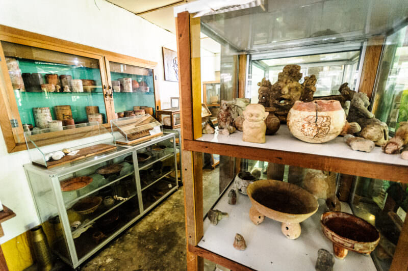 Display cases in the Radio Petén Island museum showing Maya pottery, incense burners, and ceremonial vessels on glass shelves