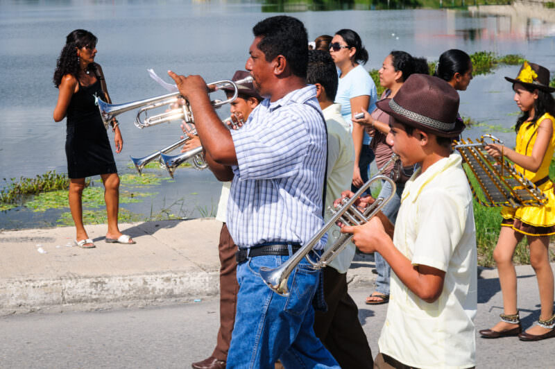 Musicians playing trumpets during the Guatemalan Independence Day parade along Lake Petén Itzá, with marchers and spectators in the background