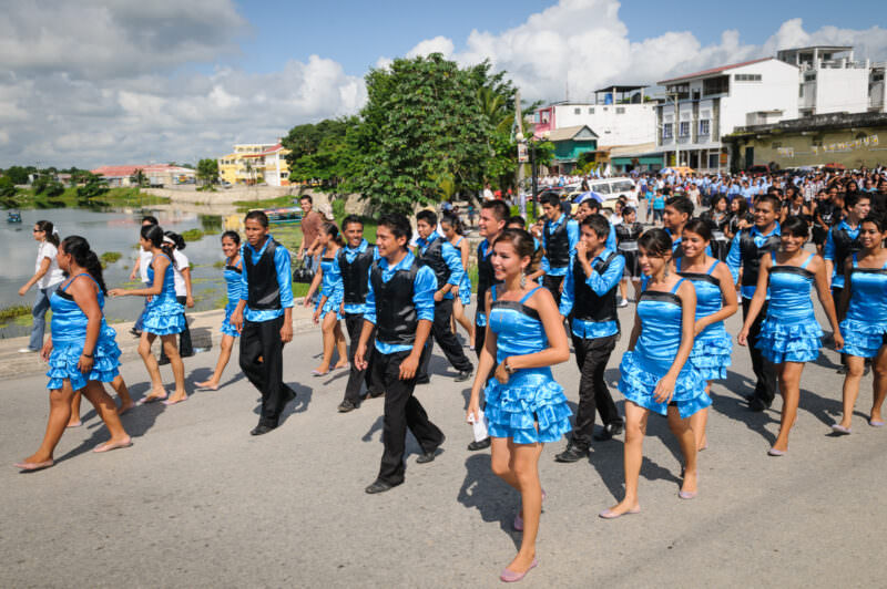 Young men and women in bright blue ruffled costumes marching in the Guatemalan Independence Day parade along the lakeside causeway