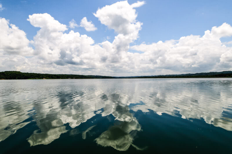 Clouds mirrored perfectly on the glassy surface of Lake Petén Itzá, with tree-lined shores visible on the horizon