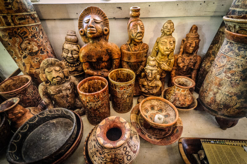 Maya ceramic figurines, vessels, and pottery displayed on museum shelves at Radio Petén Island