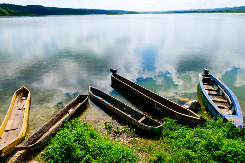 Traditional wooden canoes resting on the reedy shore of Lake Petén Itzá, their reflections mirrored in the still water beneath distant green hills
