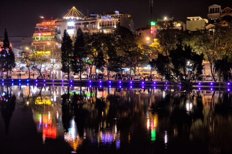 Illuminated Old Quarter rooftop cafes and neon signs reflected in Hoan Kiem Lake at night