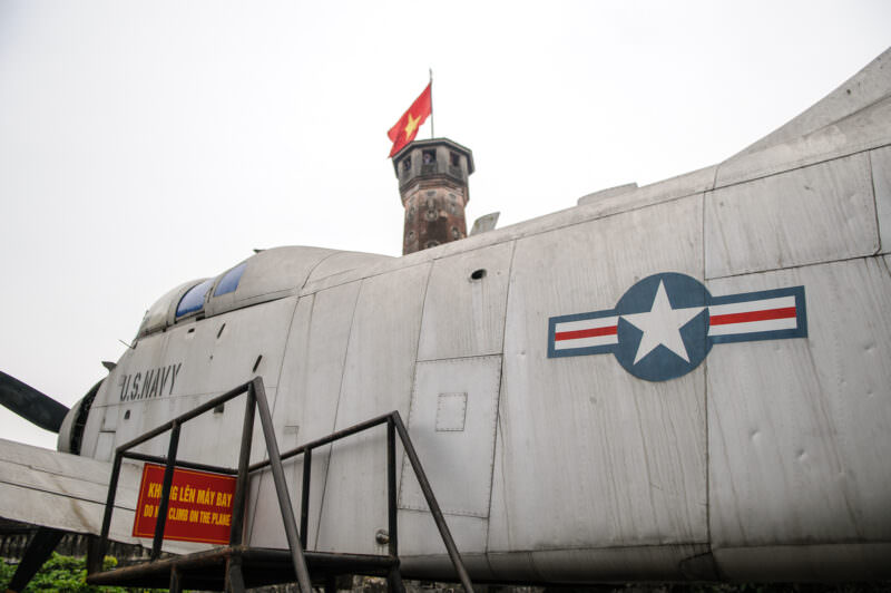 Captured U.S. Navy aircraft fuselage with visible star roundel displayed beneath the Hanoi Flag Tower