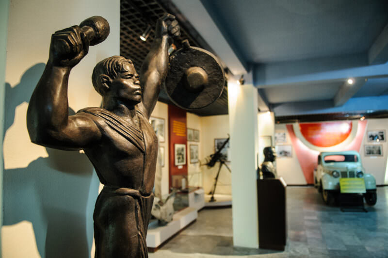 Bronze socialist-realism statue of a man raising a gong, part of a gallery display at the museum