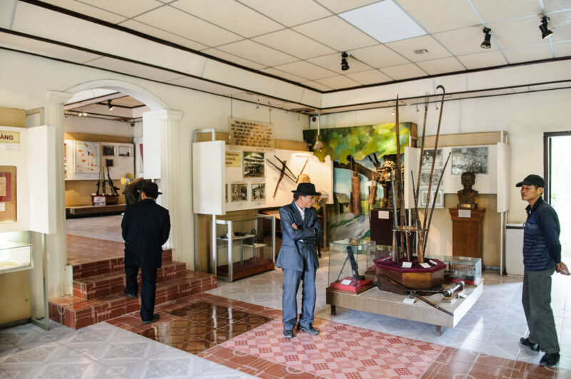 Visitors in suits view a case of forged farming tools and polearms in a museum exhibit hall