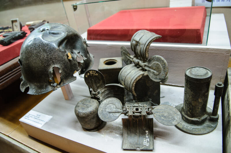 Shrapnel-pierced French steel helmet displayed with rusted ordnance fragments in a museum case