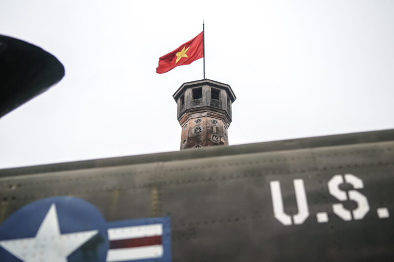 Hanoi Flag Tower's octagonal top and red flag rising behind a captured U.S. aircraft fuselage