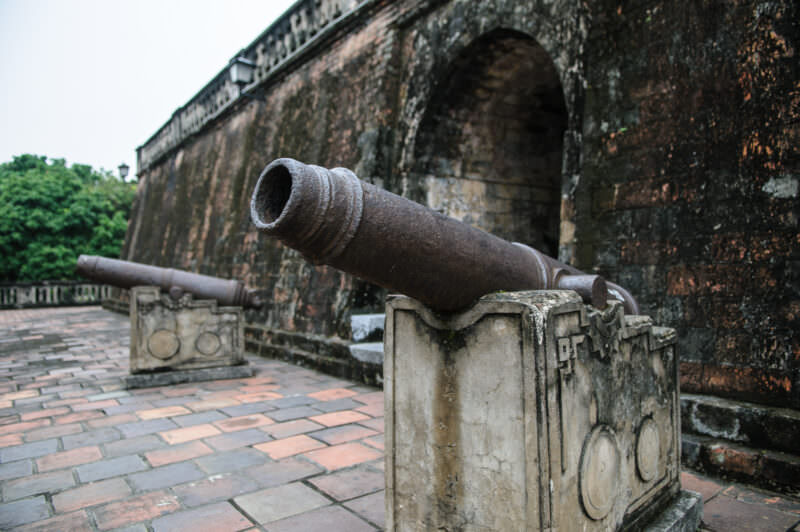 Rusted cast-iron cannons on stone mounts beside the arched brick base of the Hanoi Flag Tower