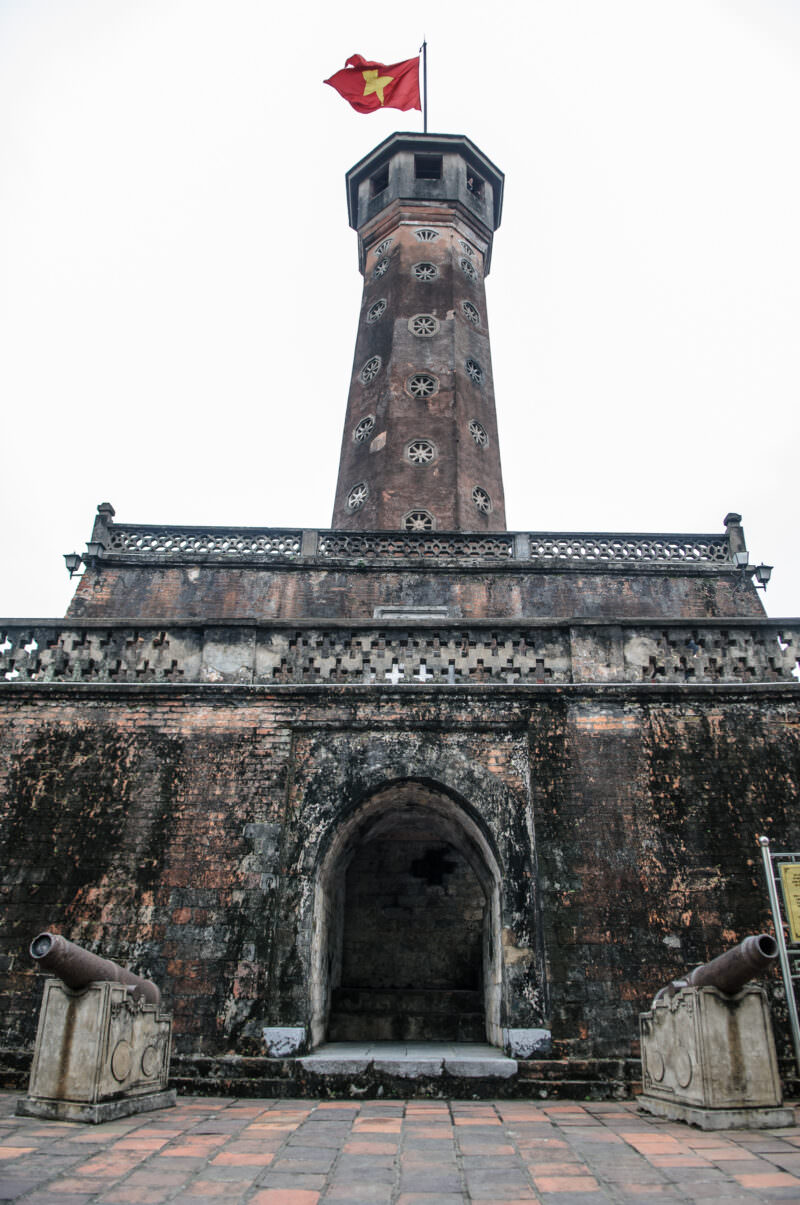 Hanoi Flag Tower's octagonal brick column and flag seen from ground level above its fortified base
