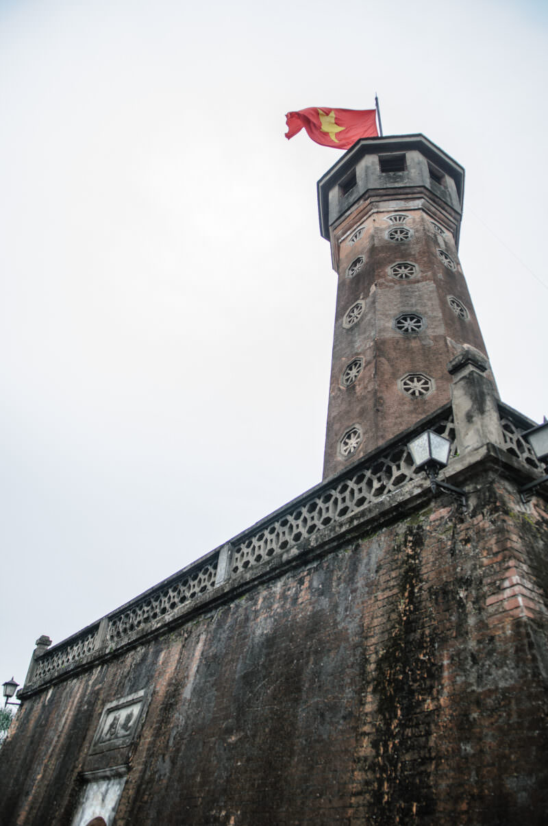 Weathered octagonal Hanoi Flag Tower with the national flag flying above its tiered brick base
