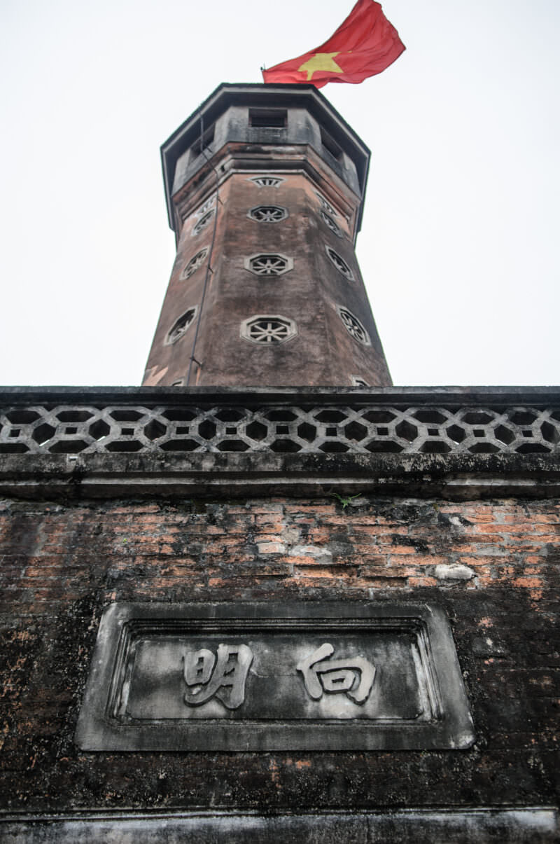 Hanoi Flag Tower's brick base with carved Hán characters reading Hướng Minh above weathered stonework