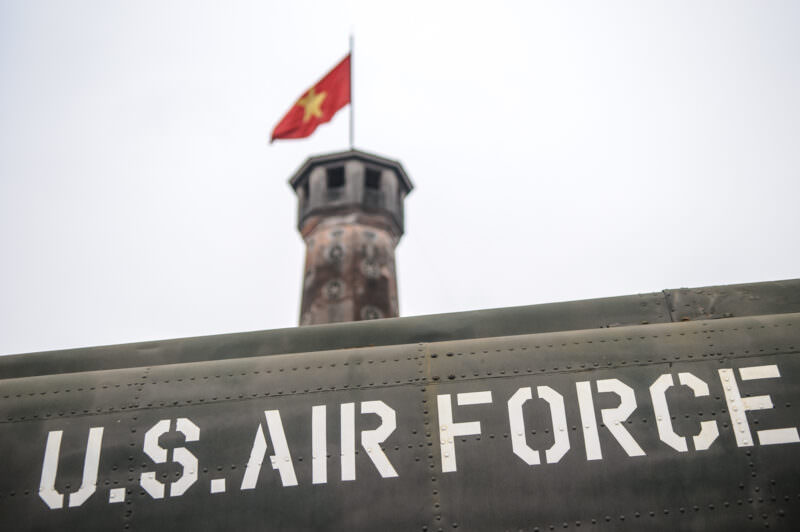 Riveted U.S. Air Force fuselage lettering framed beneath the distant Hanoi Flag Tower and flag
