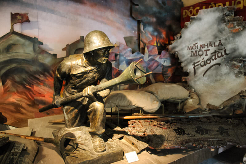 Bronze statue of a Viet Minh soldier gripping a lunge mine in a barricaded-street diorama