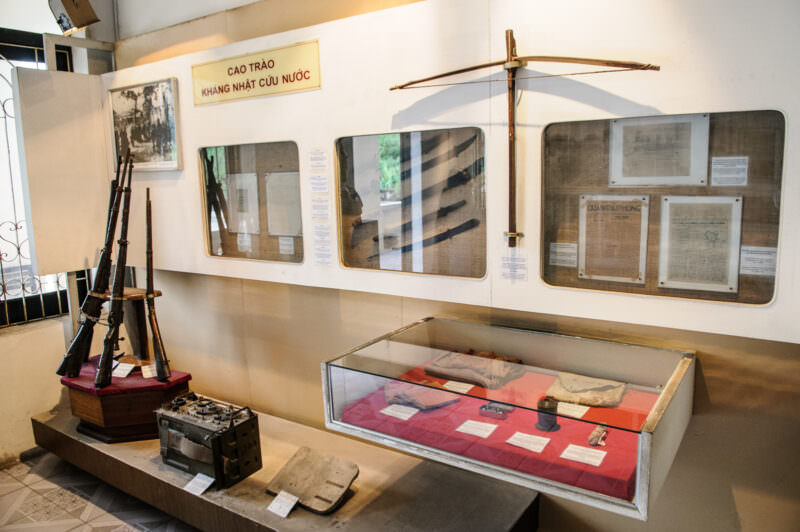 World War II exhibit at the Vietnam Military History Museum showing rifles, a crossbow, and archival documents