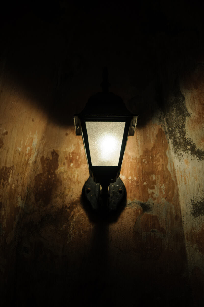 A lit wall lantern casting light on the weathered brick interior of the Hanoi Flag Tower