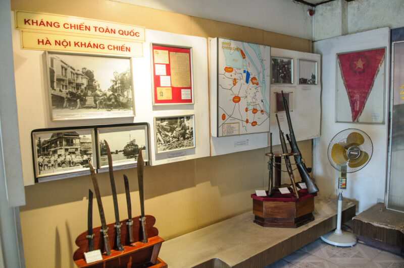 Museum wall display of Viet Minh swords, rifles, tactical maps, and photos from the Battle of Hanoi