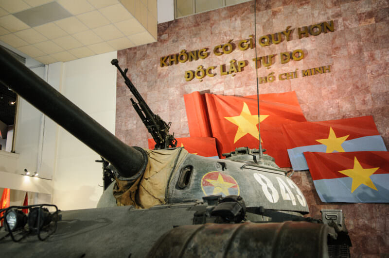 Turret of tank 843 displayed before a gold Ho Chi Minh inscription and Vietnamese flags