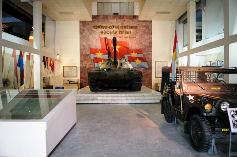 Gallery pairing a Soviet-built tank and a captured U.S. jeep beneath a red flag mural wall