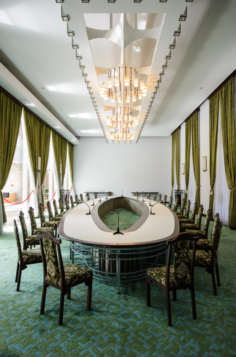 Oval conference table with microphones beneath a sculptural chandelier in an upper-floor room of Reunification Palace