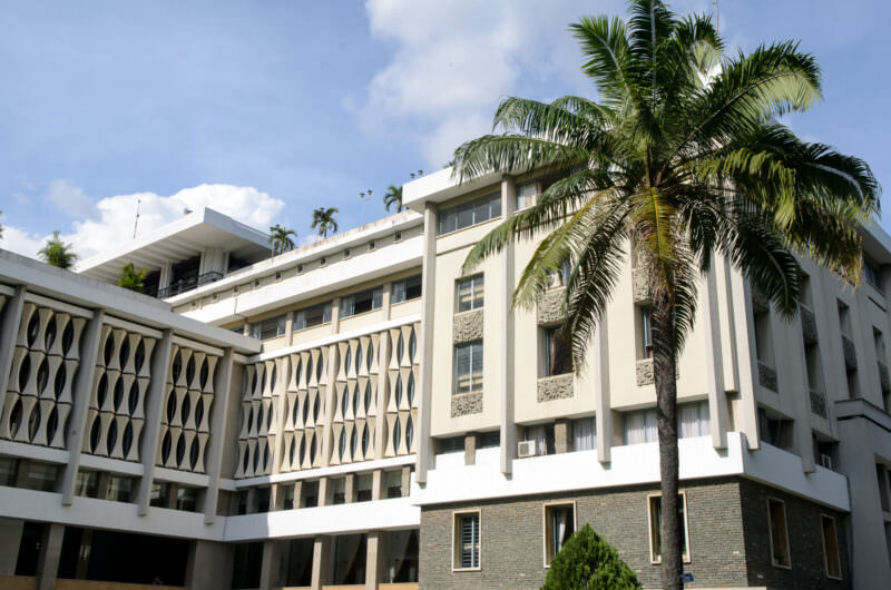 Palm tree framing Reunification Palace's concrete brise-soleil facade and modernist upper floors