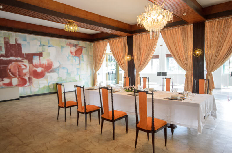 Formal dining table with orange chairs beneath a large abstract mural in Reunification Palace's private dining room