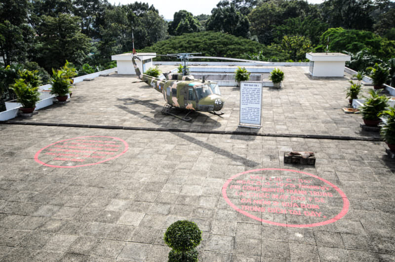 Camouflaged UH-1 helicopter on Reunification Palace's rooftop pad beside painted bomb-impact markers