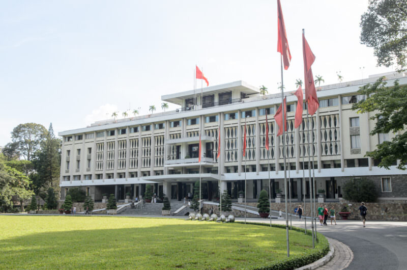 Reunification Palace's white modernist facade and red flags viewed across its oval front lawn