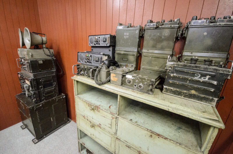 Rows of vintage olive-drab military radio equipment on a cabinet in Reunification Palace's bunker