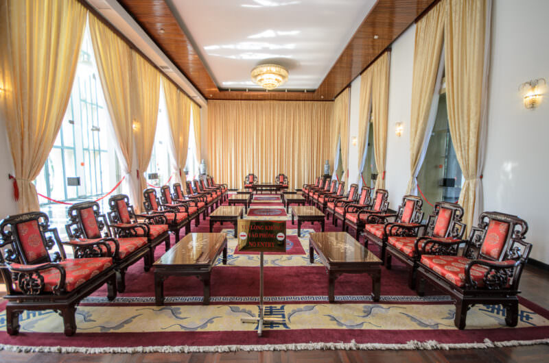 Symmetrical rows of carved red armchairs on a patterned rug in a formal reception hall at Reunification Palace