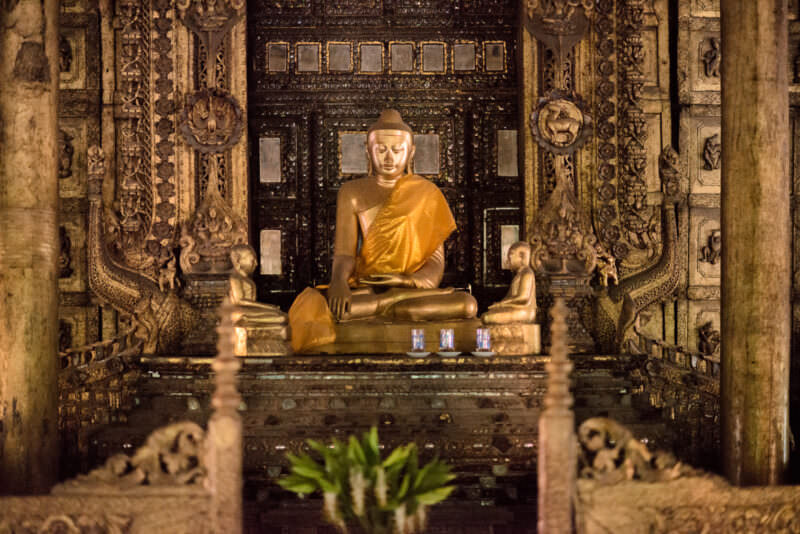 Gilded Buddha in bhumisparsha mudra enthroned within darkened carved teak interior of Shwenandaw Monastery