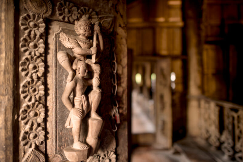 Deep-relief teak panel inside Shwenandaw Monastery depicting demon seizing human figure, Jataka narrative motif