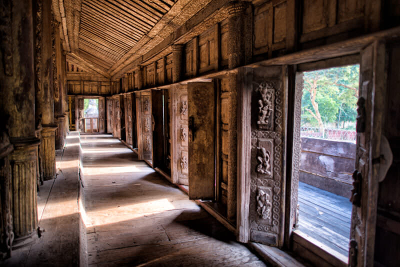 Carved teak doors lining veranda corridor at Shwenandaw Monastery, deep-relief figural panels in shadowed wooden interior