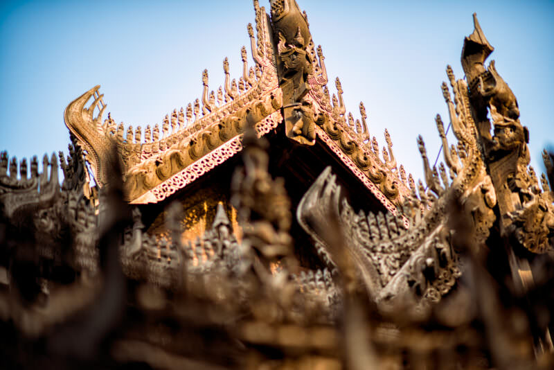 Shwenandaw Monastery tiered pyatthat roofline bristling with carved teak finials, naga serpents, and mythical figures against clear sky