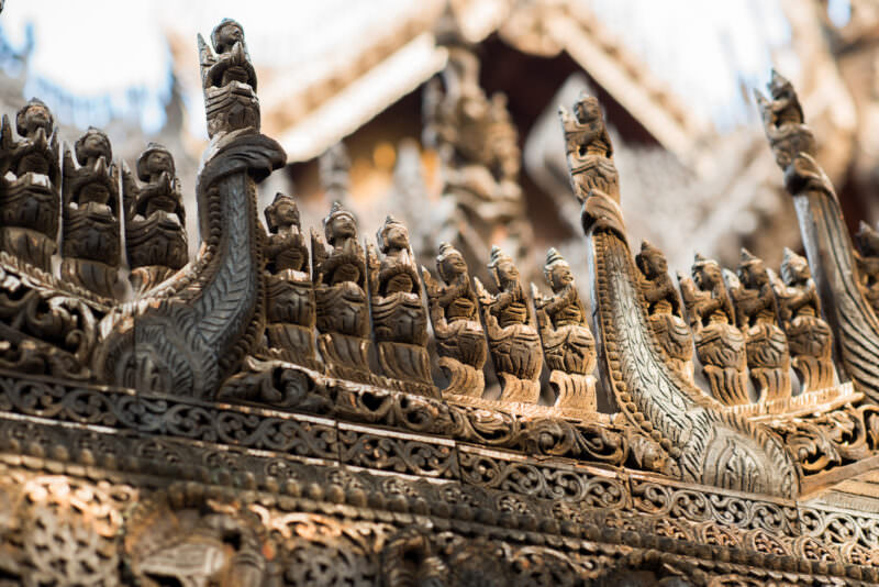 Weathered teak figures crowding eave-board of Shwenandaw Monastery, gilding stripped to bare silver-grey wood