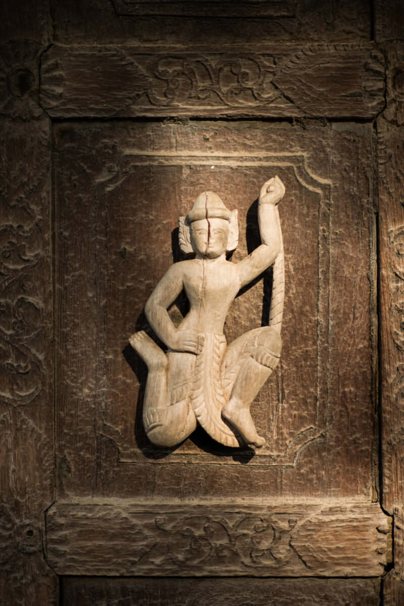Newly carved pale teak court dancer on door panel at Shwenandaw Monastery, contrasting with silver-grey surrounding wood