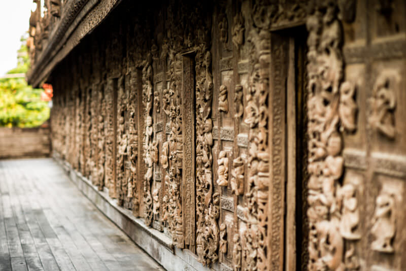 Jataka panels and mythical figures covering exterior veranda wall at Shwenandaw Monastery, receding in perspective along teak walkway