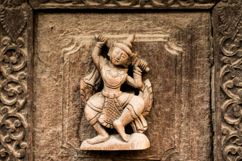 Court dancer carved in high relief on weathered teak door panel at Shwenandaw Monastery, grain-exposed surface