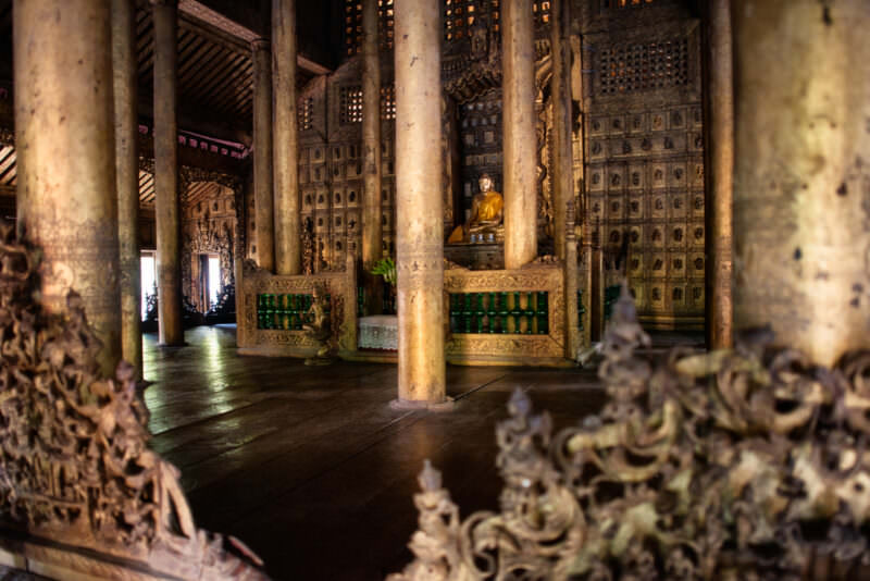 Gilded Buddha at central shrine of Shwenandaw Monastery seen through massive teak columns, Jataka panels covering walls