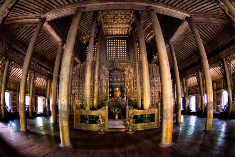 Fisheye view inside Shwenandaw Monastery, teak columns radiating from central Buddha shrine, carved walls and ceiling structure