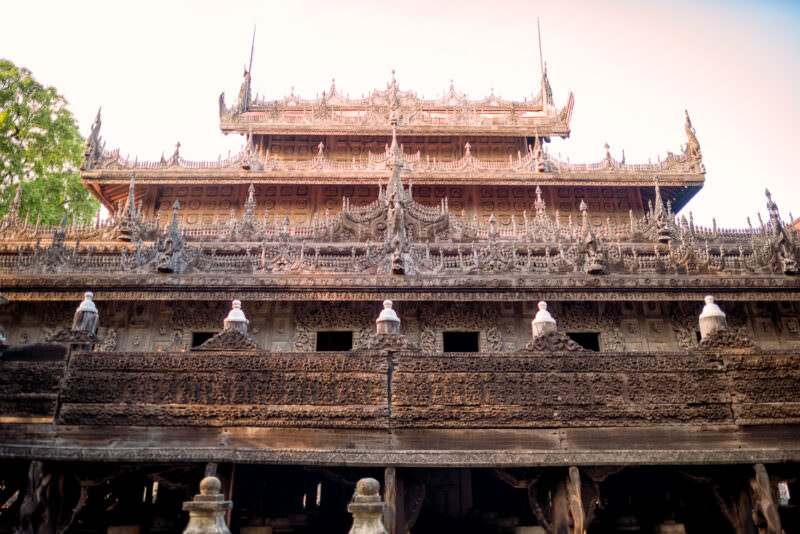Shwenandaw Monastery upper facade with tiered deep-relief teak carving, finials, and crested eaves beneath pyatthat roof