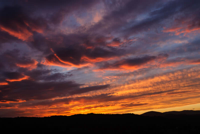 Dramatic altocumulus clouds blazing orange and red at sunset over the dark silhouetted mountain ranges near Towamba