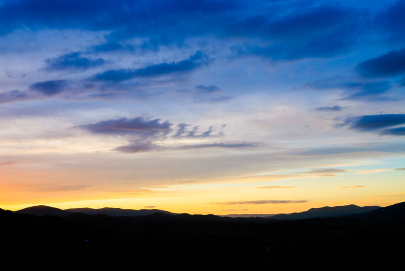 Sunset gradient from yellow at horizon to deep blue overhead across the silhouetted peaks of the Great Dividing Range