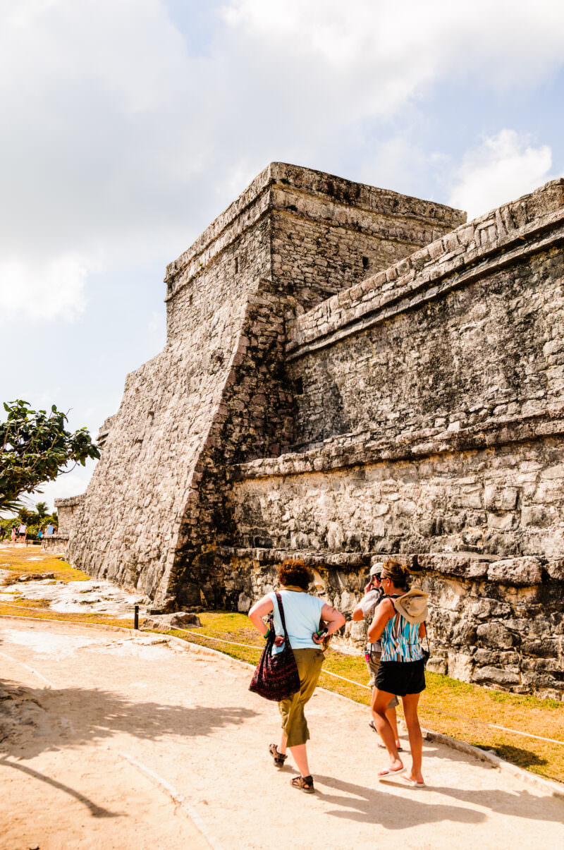 El Castillo pyramid at Tulum viewed from below, its massive limestone base and top temple against a pale sky