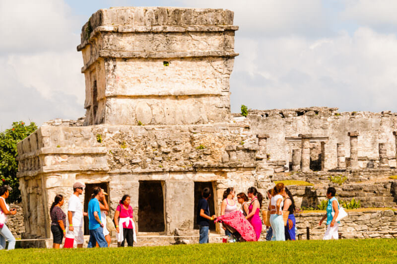 Temple of the Frescoes at Tulum, its weathered limestone facade with columned lower level and upper tower, visitors approaching