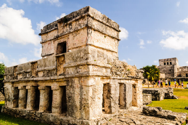 Temple of the Frescoes at Tulum, its weathered stone tower and columned lower level with carved details visible in sunlight